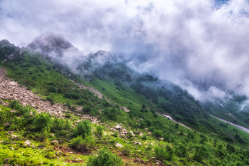 The green slopes of high mountains are hidden in clouds and fog. Melting snow in high mountains in summer