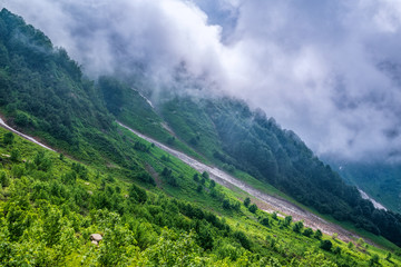 The green slopes of high mountains are hidden in clouds and fog. Melting snow in high mountains in summer