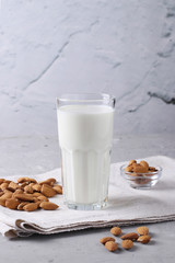 Fresh almond milk in transparent glass and almonds on gray concrete background, Healthy vegan milk replacer, Vertical format, Closeup