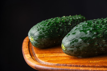 Close-up of two whole wet cucumbers on wooden board, black background, horizontal, with copy space