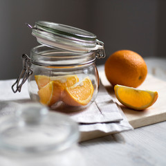 Sliced orange slices in a jar with a lid. On the table there is a cutting board with a gray napkin and orange. Making jam or juice.