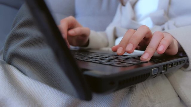 Hands of woman with nude manicure typing working on laptop sitting on couch, freelance distant work on quarantine. Coronavirus pandemic. Self empoyed businesswoman, COVID-19 epidemic. Wearing suit.