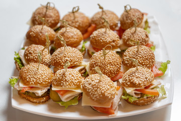 Mini chicken burgers with cheese and tomatoes on a white plate. Bonded with beautiful bamboo sticks.
