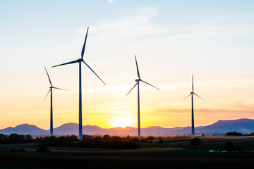 4 wind turbines stand in a small wind farm in the Rhine valley near Landau in front of the silhouette of the Palatinate Forest.