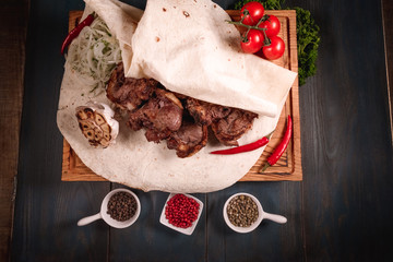 Appetizing fried meat lies on a wooden tray, among the seasonings. Studio photography of food in the cooking industry, dark background