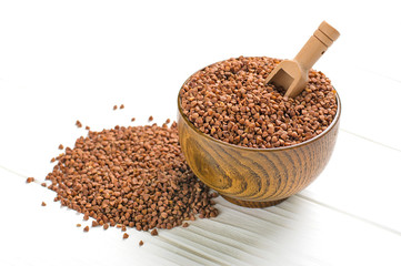 brown buckwheat grains in wooden bowl on isolated white background Healthy food, superfood concept