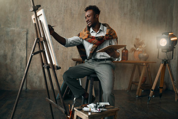 Smiling painter with brush and palette at easel