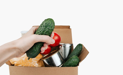 Box with products. Food donation. Vegetables, cereals and canned goods in a cardboard box. Cucumber in the hand.