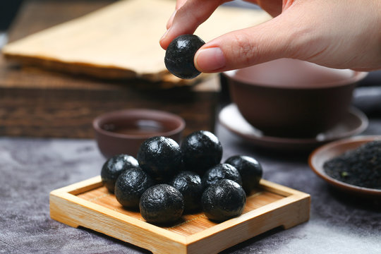 woman hand holing black sesame ball on bamboo plate with tea