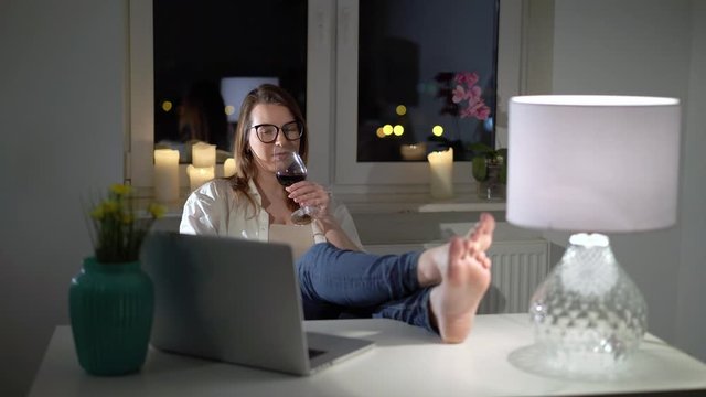 Young woman working at computer laptop at home office in the evening with wine