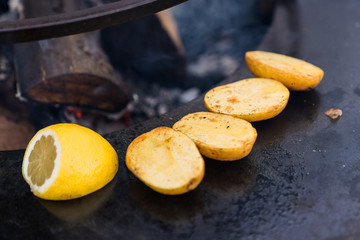 Pieces of sliced potatoes and lemon grilled on a black surface
