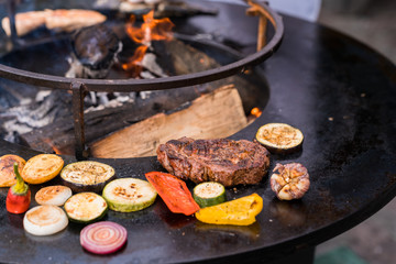 Beef steak and sliced vegetables on a round grill surface.