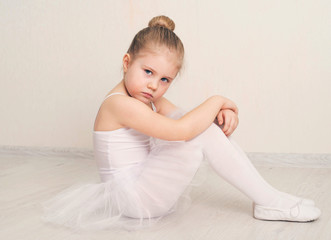Cute little girl dreams of becoming a ballerina. Child girl in a white  tutu sitting. Baby girl studying practicing ballet.