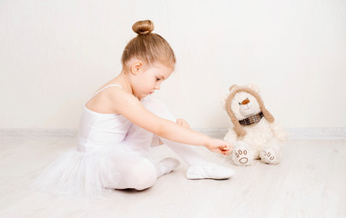 Cute little girl dreams of becoming a ballerina. Child girl in a white  tutu tying her ballet slippers. Baby girl studying practicing ballet. © Polina Ponomareva
