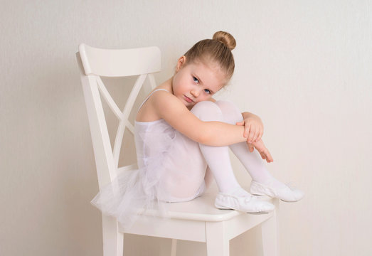 Cute little girl dreams of becoming a ballerina. Child girl in a white  tutu sitting. Baby girl studying practicing ballet.