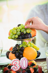 Woman hand taking grape from high plate of fruits. Close up