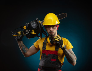 a guy in protective overalls with a chainsaw on a dark background
