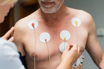 Old man during a cardiac diagnostic test. Woman's hand putting detector on a chest