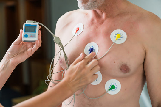 Old man during a cardiac diagnostic test. Woman's hand putting detector on a chest and measure with devise
