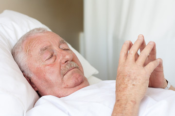 elderly man with closed eyes lying in hospital bed