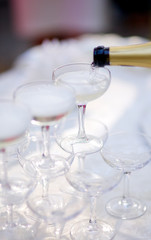 Champagne is poured into a white transparent glass from a bottle. On a Sunny festive summer day, glasses sparkle in the sun.