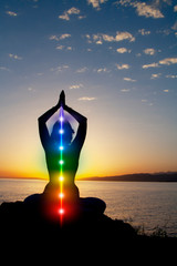 Silhouette of woman sits in a lotus pose on beach sunset view, glowing seven all chakra. Kundalini energy. girl practicing yoga meditation outdoors