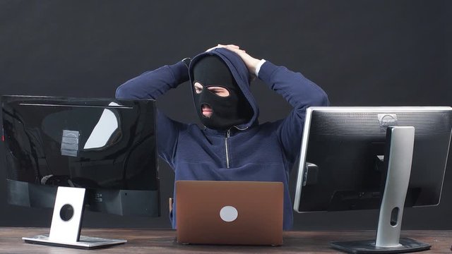Young hacker man in balaclava, sit in hood of pullover. Professional programmer male hiding face behind a mask, hack anonymously, man engaged in crime.