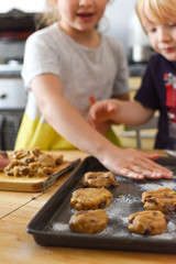 Kids making cookies in kitchen placing dough on tray for cooking at home