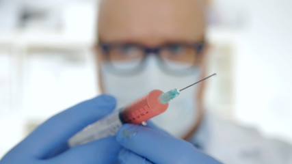 Doctor Wearing Protecting Gloves and Face Mask Keeping in His Hand an Injection with a Vaccine, Antidote, and Treatment for Covid-19 Virus Pandemic