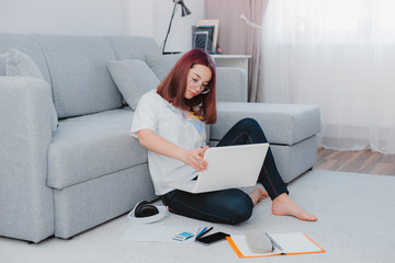 young girl teenage schoolgirl lying floor living room sofa student studying home working with her laptop doing homework.