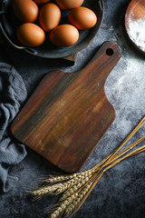 blank wooden cutting board and eggs and dry wheat on dark background