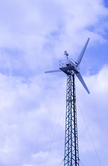 a wind turbine generates electrical energy against a cloudy blue sky. Vertical photo