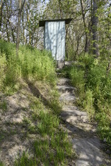 Naklejka premium Wooden toilet in the forest, on a raised platform. Entrance steps up. Beautiful wildlife in spring.