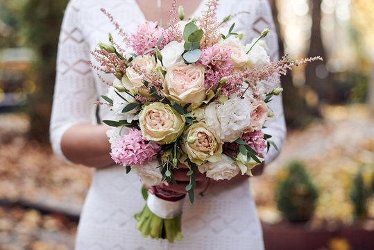 Close-up picture of bride's hands, holding beautiful white and pink flower rose bouquet. Close-up picture of wedding decorations details.