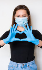 Young woman in medical mask and gloves shows a heart sign.