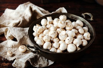 Fresh raw champignons in an iron bowl on a dark wooden table, rustic style