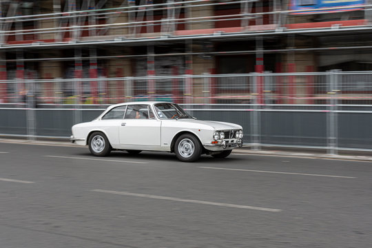Panning of a classic white car running on the avenue of the city.