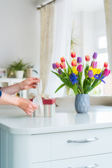 Female hands are opening gift box on marble table with colorful spring flowers bouquet in vase. Light interior room. Happy birthday, women's day, Mother's Day background. Vertical card. Copy space.