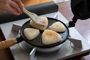 自宅で作る焼きおにぎり　焼きおにぎり器で焼いているおにぎりに刷毛でだし醤油を塗る様子