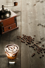 Cappuccino decorato con cacao su sfondo tavole di legno e un macinino, sparsi sul tavolo diversi...