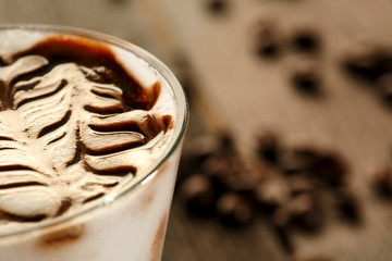 Cappuccino decorato con cacao su sfondo tavole di legno, sparsi sul tavolo diversi chicchi di caffè
