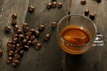 tazzina di caffè in vetro con dei chicchi sopra delle tavole di legno