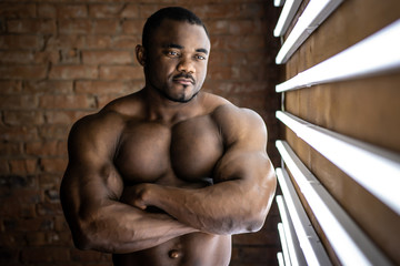 Strong afroamerican athletic man with perfect shape musculs on brick background next to daylight lamps