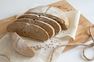 Loaf of sliced rye multigrain bread on wooden cutting board decorated with natural fabric closeup. Concept of fresh pastry, healthy food.