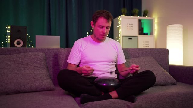 a man sits at home and plays on the hapi drum