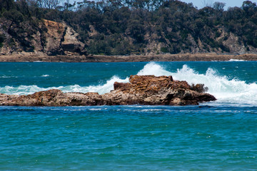Tomakin Australia, view across bay with waves breaking over rocky outcrops and hill with trees in background