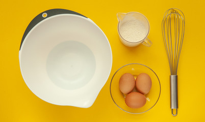 Whisk and a plastic cup for whipping on a yellow background.