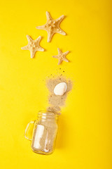 Starfishes and seashells, glass with sand on yellow background