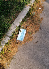 Disposable blue medical mask thrown on a sidewalk during the coronavirus outbreak, environmental pollution 