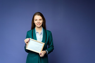 A smiling girl with white frame is on the blue background. Attractive girl is holding a white frame on background
